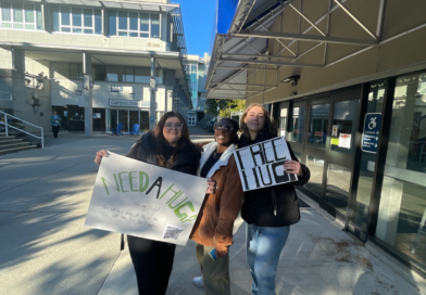Three psychology students holding Free Hugs signs on VIU campus.