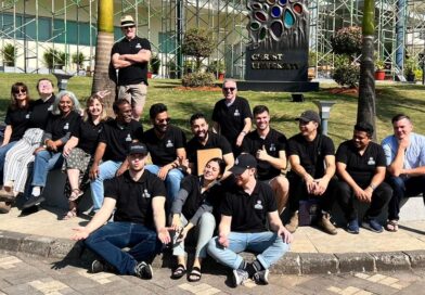 Team of 20+ youth in black t-shirts on lawn of building in India.