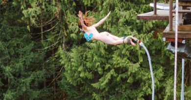 Woman mid-air bunny jumping naked against forest of trees.