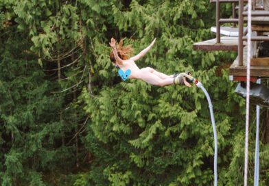 Woman mid-air bunny jumping naked against forest of trees.