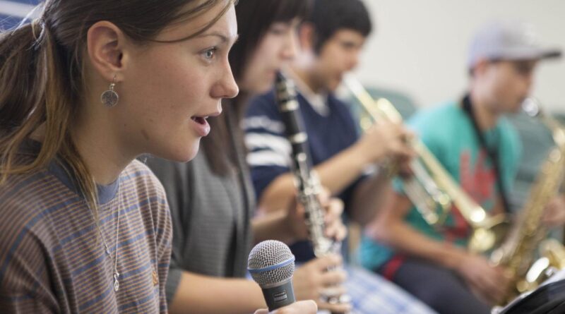 3 20-something students holding a mic, clarinet or trumpet each.