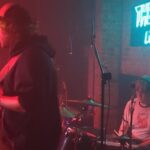 woman drummer and male guitartist on small dark stage