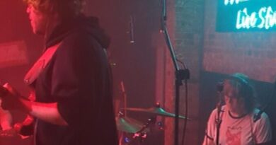 woman drummer and male guitartist on small dark stage