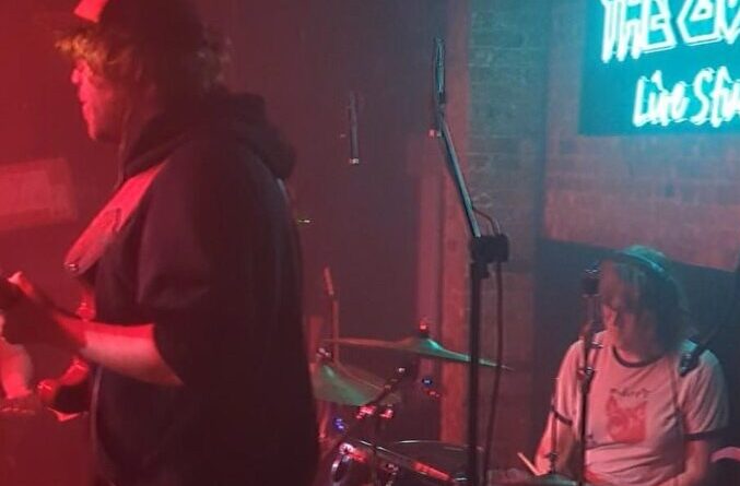 woman drummer and male guitartist on small dark stage