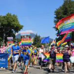 People of all ages in multicoloured outfits marching on the street for the Pride festival.