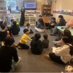 Korean children sitting on the floor in a classroom with two female instructors at the front of the room.