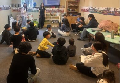 Korean children sitting on the floor in a classroom with two female instructors at the front of the room.