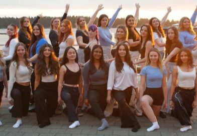 Two rows of women posing in dance wear on a pier outdoors