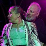 Man gripping womans arms from behind and looking at her as she looks away on stage